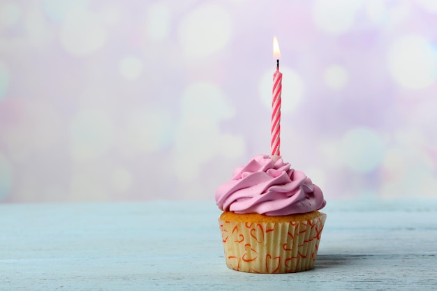 Süßer Cupcake mit Kerze auf blauem Holztisch vor verschwommenem Hintergrund