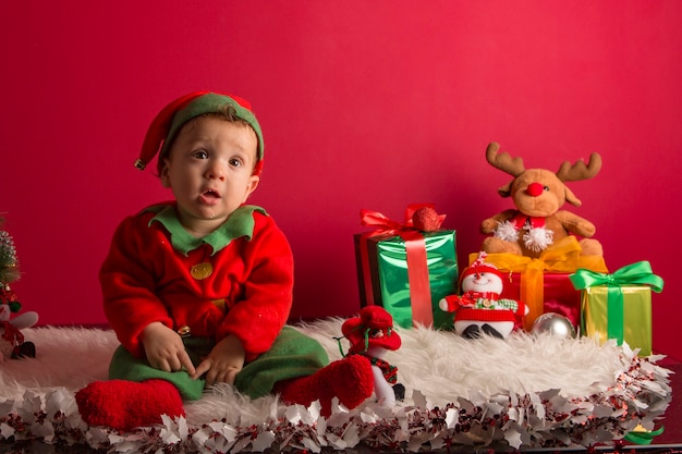 Süßer einjähriger Junge verkleidet als Elf in Weihnachtsdekoration mit Geschenken