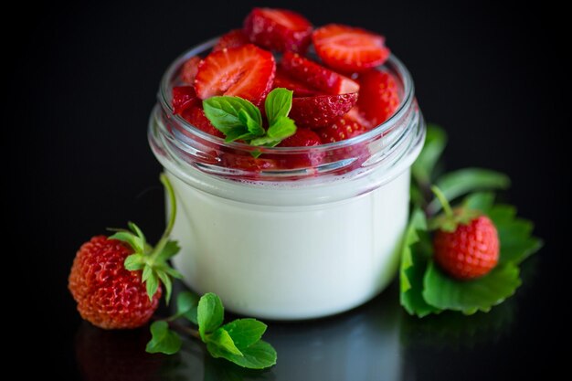 Süßer hausgemachter Joghurt mit frischen reifen Erdbeeren in einem Glas isoliert auf schwarzem Hintergrund