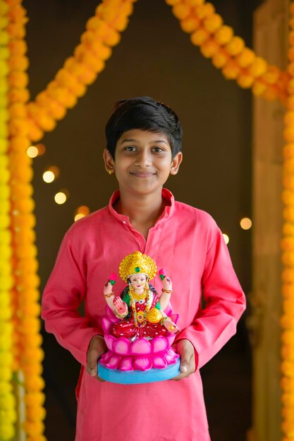 Süßer indischer kleiner Junge, der die Göttin Laxmi in der Hand hält und das Diwali-Festival feiert.