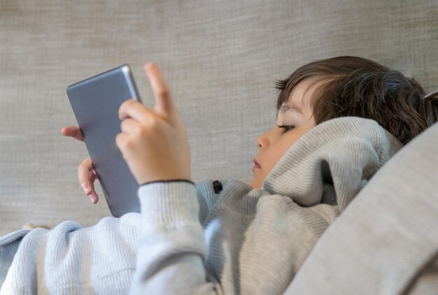 Foto süßer junge benutzt ein digitales tablet, während er zu hause auf dem sofa liegt