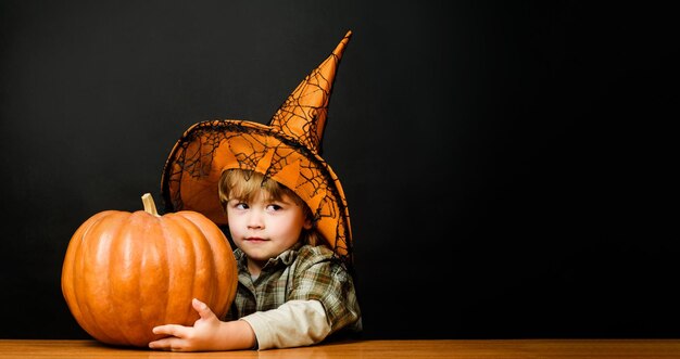 Foto süßer junge mit hexenhut mit halloween-kürbis vorbereitung für halloween-ferien thanksgiving day