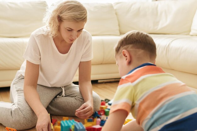 Süßer Junge und seine glückliche Mutter spielen zu Hause zusammen