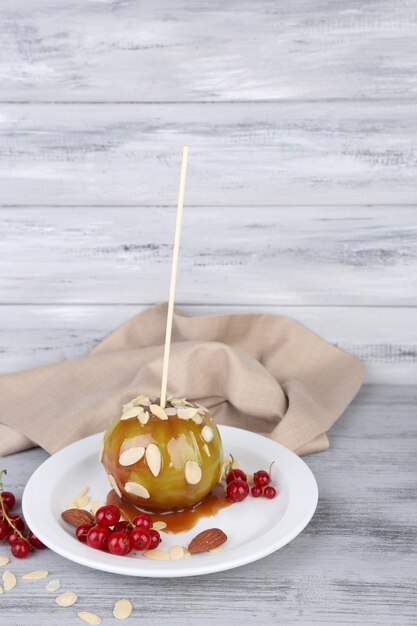 Süßer Karamellapfel am Stiel mit Beeren, auf Holztisch