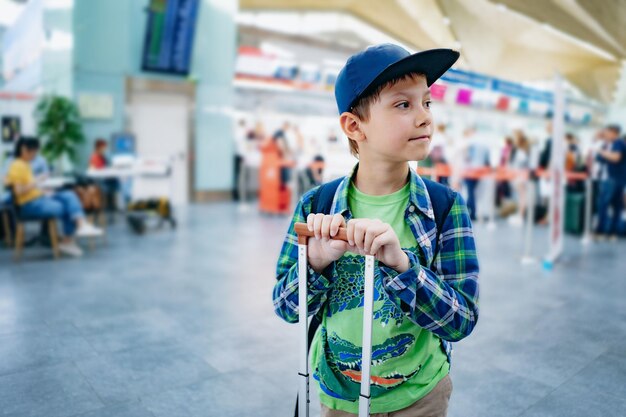 Süßer kaukasischer Junge auf dem Flughafen mit Rucksack und Koffer Reisekonzept