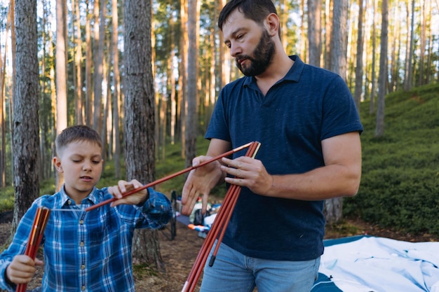 süßer kaukasischer Junge hilft Vater beim Aufbau eines Zeltes Familiencamping-Konzept