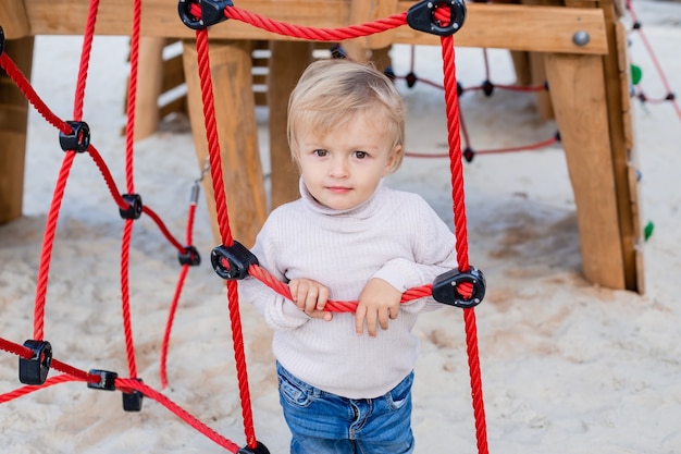 Süßer kleiner blonder Junge in einem Strickpullover spielt im Herbst in der Kinderstadt im Stadtpark