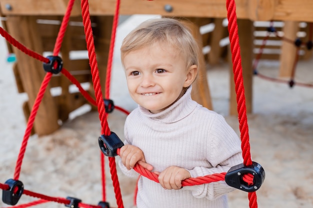 Süßer kleiner blonder Junge in einem Strickpullover spielt im Herbst in der Kinderstadt im Stadtpark