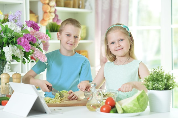 Süßer kleiner Bruder und Schwester schneiden gemeinsam Gemüse für Salat in der Küche