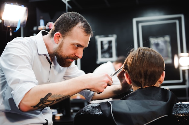 Süßer kleiner Junge bekommt Haarschnitt durch Friseur im Friseursalon.