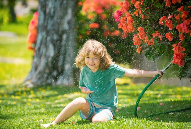 Süßer kleiner Junge, der Blumen im Garten am Sommertag gießt Kinderbauer mit Gartenschlauch in planti