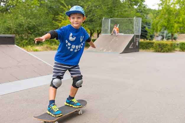 Süßer kleiner Junge, der in einem Skatepark Skateboard fährt und seine Haltung auf dem Brett mit einem glücklichen Lächeln übt