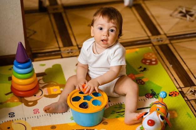 Süßer kleiner Junge, der mit bunten Lernspielzeugen auf der Spielmatte im Innenbereich spielt