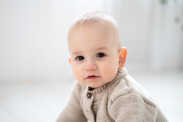 Süßer kleiner Junge, großes Porträt eines Kindes mit braunen Augen und blonden Haaren in einem pastellfarbenen Strickanzug