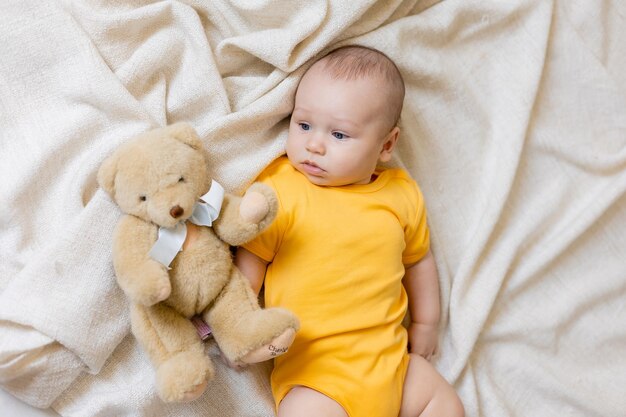 süßer kleiner junge im gelben körper, der auf decke mit teddybär, karte, platz für text, gesundheit liegt