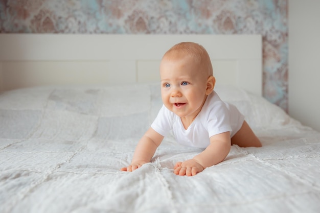 Süßer kleiner Junge in einem weißen Body, der im Schlafzimmer auf dem Bett krabbelt, das Konzept der glücklichen Mutterschaft