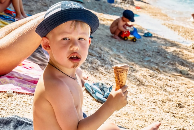 Süßer kleiner Junge mit Panamahut isst Schokoladeneis am Strand