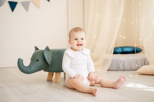 Süßer kleiner Junge oder Mädchen in einem hellen Kinderzimmer mit einem Wigwam und einem spielenden Elefanten in einem weißen Baumwollbody