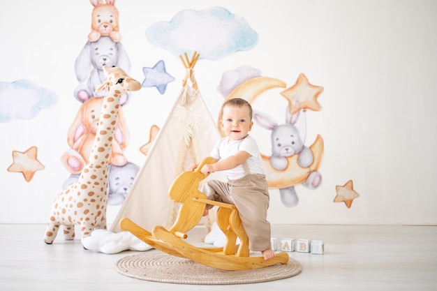 Süßer kleiner Junge reitet auf einem hölzernen Schaukelhasen im Kinderzimmer zu Hause Lernspielzeug für Kinder