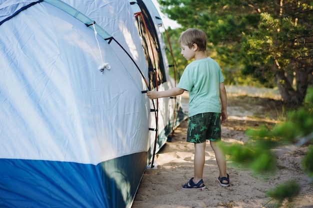 Süßer kleiner kaukasischer Junge, der hilft, ein Zelt aufzustellen Familiencampingkonzept