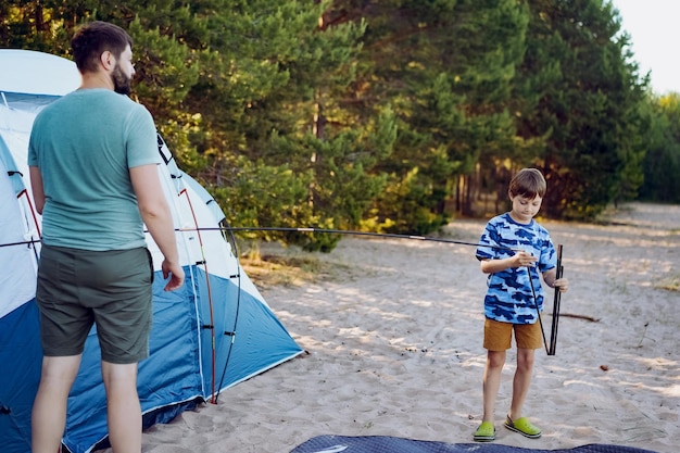 Süßer kleiner kaukasischer Junge, der hilft, ein Zelt aufzustellen Familiencampingkonzept