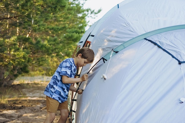 Süßer kleiner kaukasischer Junge, der hilft, ein Zelt aufzustellen Familiencampingkonzept