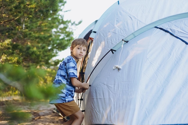 Süßer kleiner kaukasischer Junge, der hilft, ein Zelt aufzustellen Familiencampingkonzept