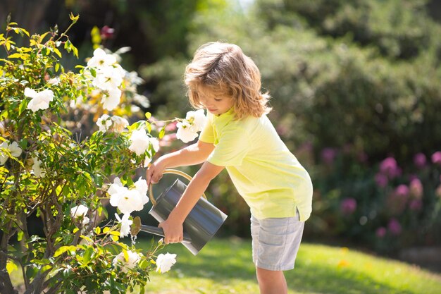 Süßer Kleinkindjunge, der am sonnigen Sommertag Pflanzen im Garten gießt