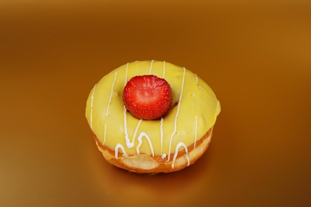 Süßer Krapfen in gelber Glasur mit roten Erdbeeren auf goldenem Hintergrund Nahaufnahme eines süßen Desserts