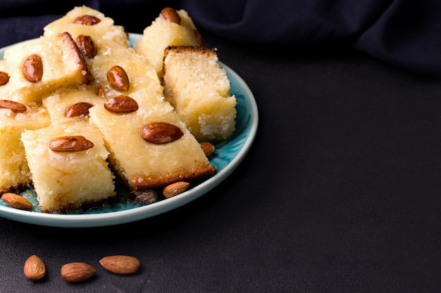 Süßer Kuchen des orientalischen Gerichts mit Grieß, Cola-Chips und Busbus-Nüssen auf einem schwarzen Hintergrund