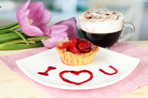 Süßer Kuchen mit Erdbeeren und Soße auf Teller mit Kaffee auf hellem Hintergrund