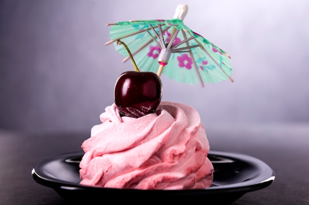 Süßer rosa Kuchen mit einer einzelnen Kirsche obenauf und einem Regenschirm in einer schwarzen Untertasse