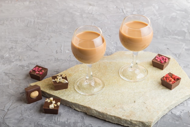 Süßer Schokoladenlikör in Glas auf einer grauen Betonoberfläche und einer Steinschieferplatte. Seitenansicht.