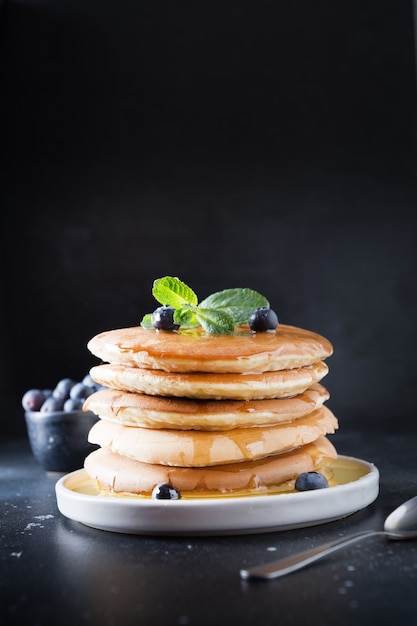 Süßer selbst gemachter Stapel Pfannkuchen mit frischer Blaubeere und Minze in der modernen Platte auf Schwarzem.