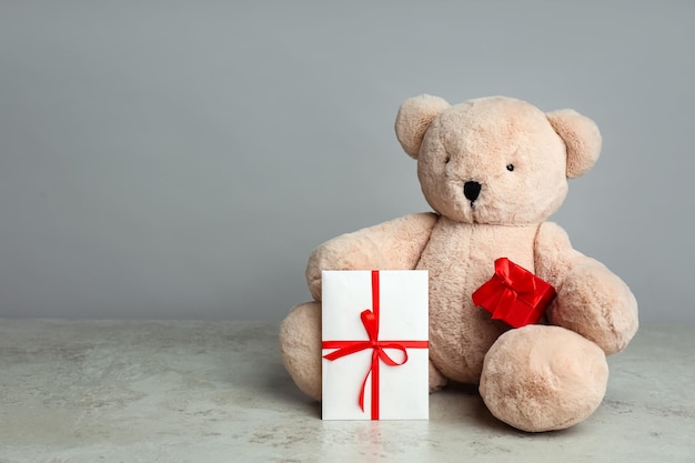 Süßer Teddybär mit Geschenkbox und Umschlag auf hellgrauem Tischplatz für die Feier des Valentinstags 39