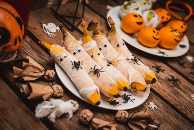 Süßer Tisch mit Früchten und Leckereien für Halloween Dekorationen Apfelbananen in Form einer Mumie mit Augen und Geisterspinnen und Kakerlaken