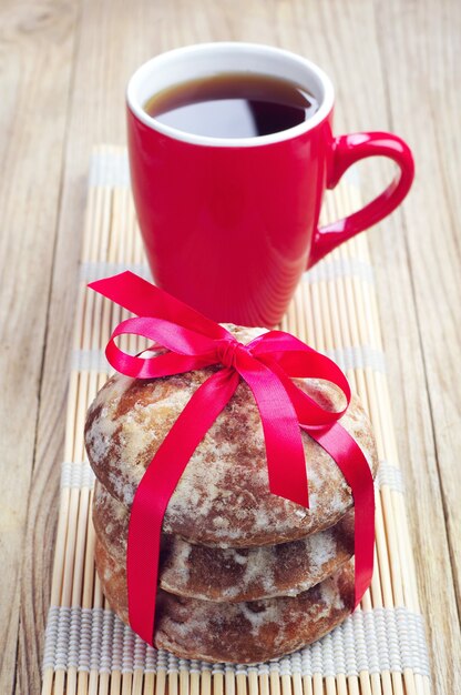 Süßer Weihnachtslebkuchen mit rotem Band und einer Tasse Tee gebunden