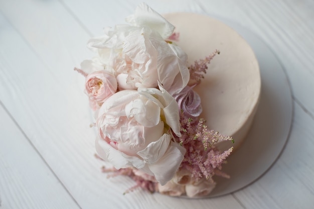 Süßer weißer Sahnekuchen rund mit rosa Rosenblüten und weißer Pfingstrose oben drauf