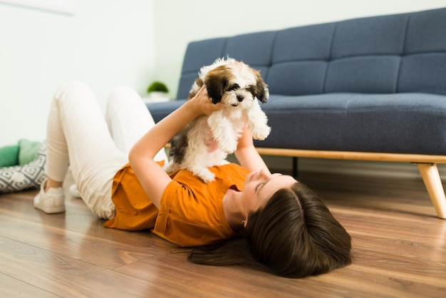 Süßer Welpe mit viel Energie, der mit einer schönen aufgeregten Frau spielt. Glückliche junge Frau, die mit ihrem entzückenden kleinen Hund auf dem Wohnzimmerboden liegt