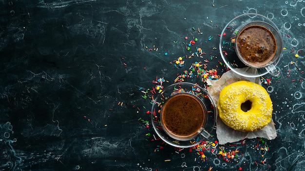 Süßer zitronengelber Donut mit einer Tasse Kaffee auf einem schwarzen Steintisch Draufsicht