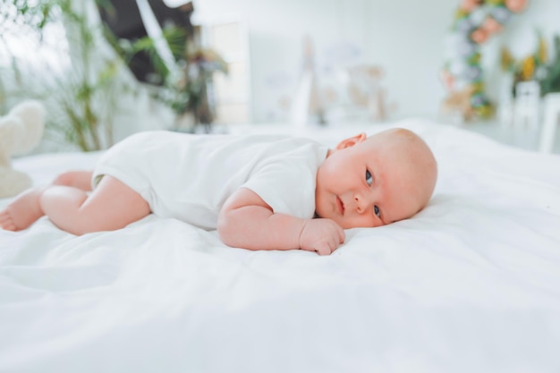 Süßes 2 Monate altes Baby, das auf dem Bett liegt, natürliche Bettwäsche, zarte Babyhaut