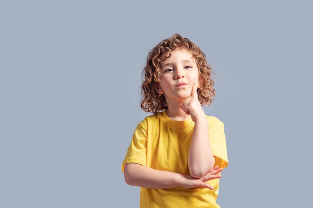 Süßes 5-jähriges Kind im gelben T-Shirt, das ihren Kopf auf Grau dreht