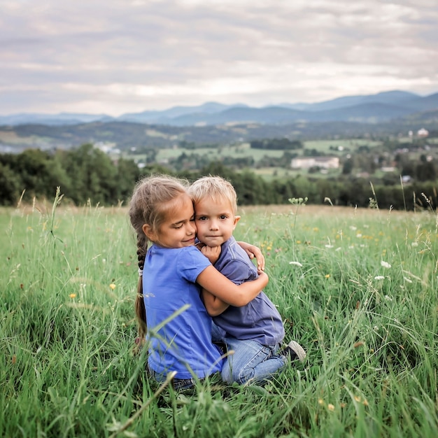 Süßes 7-8-jähriges Mädchen, das im Sommer ihre Kleinere auf den Gipfeln der Berge umarmt