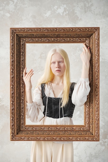 Süßes Albino-Mädchen in mittelalterlicher Kleidung, das hinter einem Bilderrahmen steht