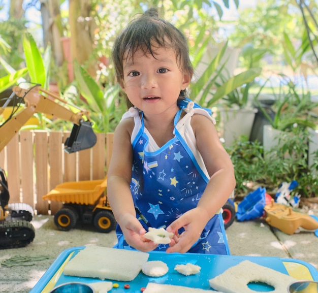 Süßes asiatisches Mädchen mit Schürze, das Spaß beim Zubereiten oder Zubereiten von Ausstecher-Sandwiches zu Hause hat