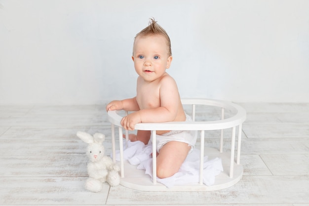 Süßes Baby auf weißem Hintergrund mit einer Frisur und großen blauen Augen in Windeln auf weißem Hintergrund mit einer Frisur, die in einem Holzkorb sitzt