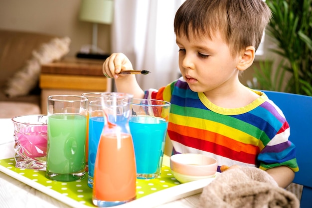 Foto süßes baby, das lernt, verschiedene farben mit wasser zu mischen und in behältern zu malen, frühe entwicklung