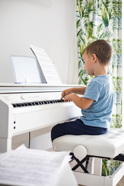 Süßes Baby, das weißes elektrisches Forte-Klavier spielt, das Tasten drückt, Kind, das an der Musikschule studiert