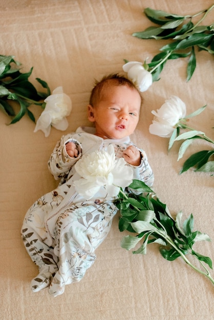 Süßes Baby in blumengemusterter Kleidung, die in Pfingstrosen liegt