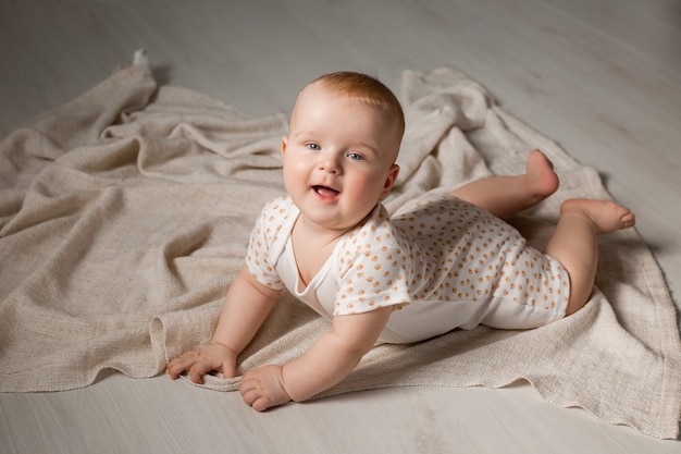 Süßes Baby in einem Body liegt auf dem Bauch auf dem Holzboden mit einer Decke zu Hause